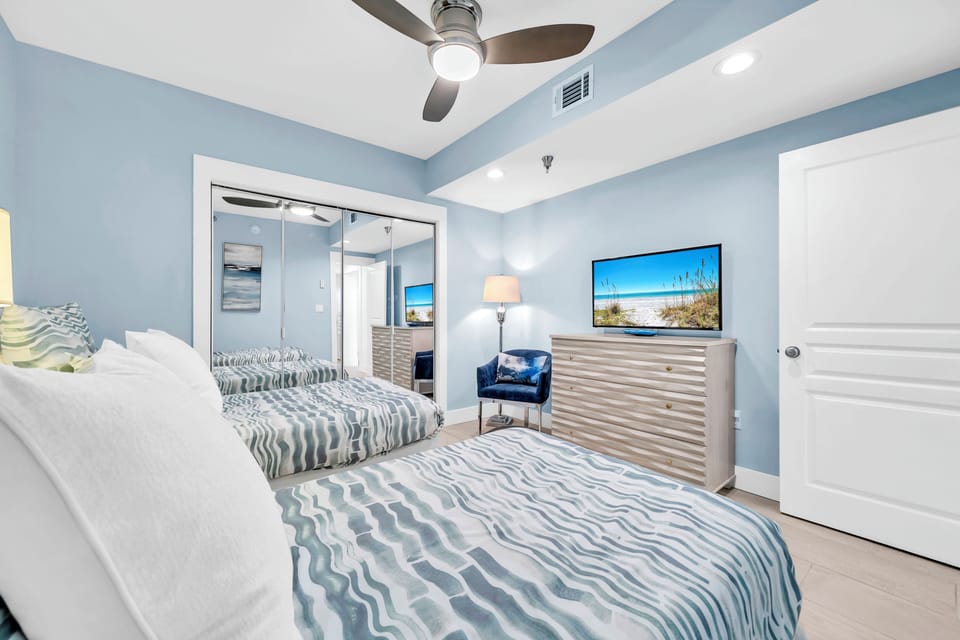 Drift off in your coastal-inspired bedroom featuring twin beds with ocean-wave linens, modern furnishings, and soothing blue walls that create a peaceful retreat.