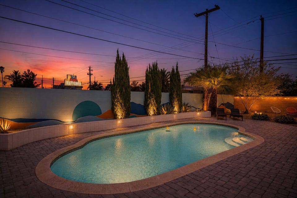 Desert-chic oasis: lit pool, mural wall, and cozy lounge seating at dusk