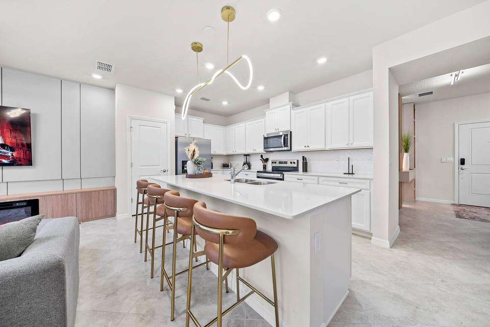 Experience a beautifully designed kitchen with sleek white cabinetry and modern stainless steel appliances. The spacious island, paired with chic brown bar stools, offers an inviting spot for casual dining and gatherings under.