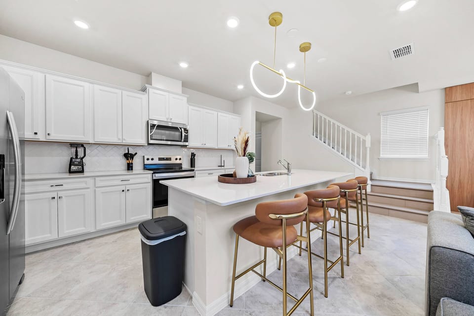 Welcome to a bright kitchen with modern white cabinetry and stainless steel appliances, perfect for your culinary adventures. The spacious island with stylish bar stools is great for casual meals or savoring your morning coffee.