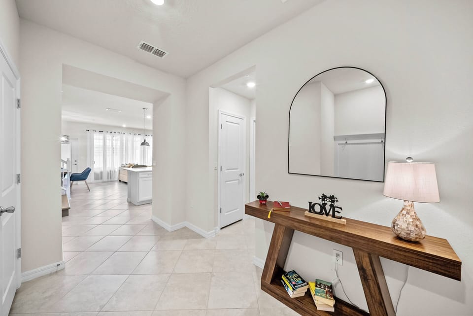 Welcome to a bright entryway with a stylish wooden console table that blends beautifully with the soft, neutral walls. A round mirror enhances the natural light, and a decorative lamp adds warmth, inviting you to discover more.