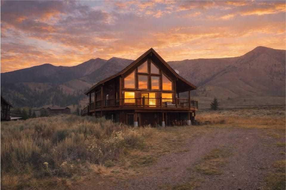 A-frame cabin glows at golden hour, mountains framing the horizon