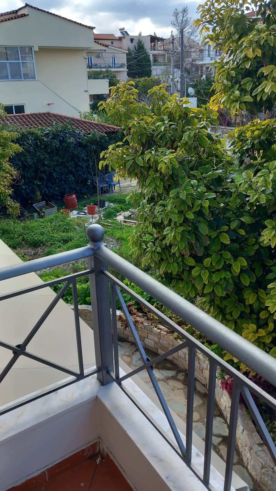 Balcony railing and surrounding greenery, showing the quiet residential setting with trees and garden.