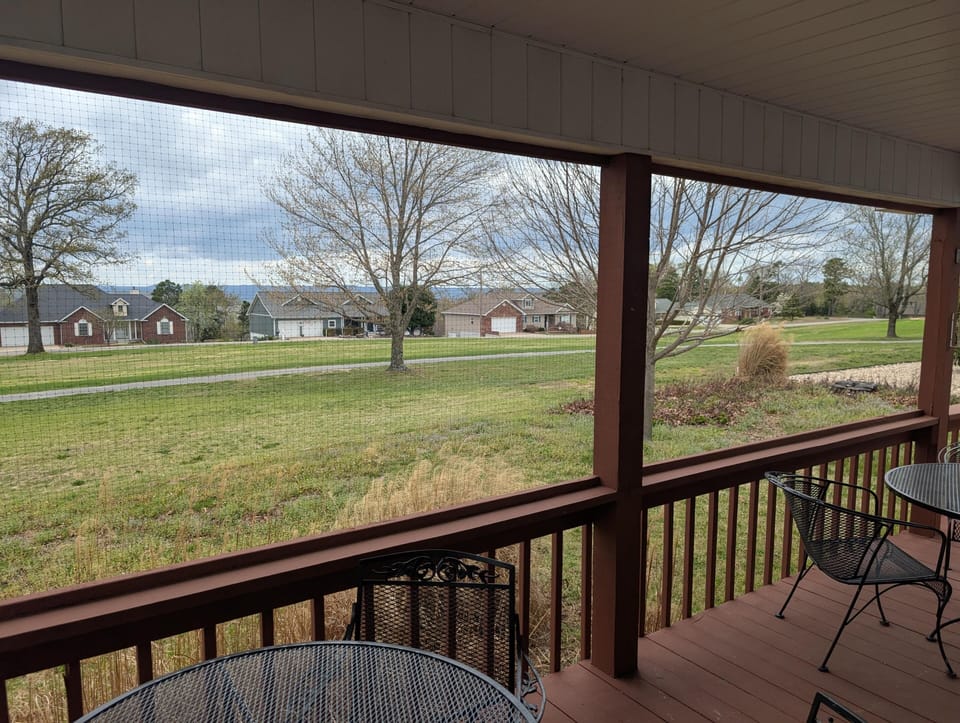 Metal mesh dining chairs surround round tables on the covered porch with rust-red wood flooring and railing.