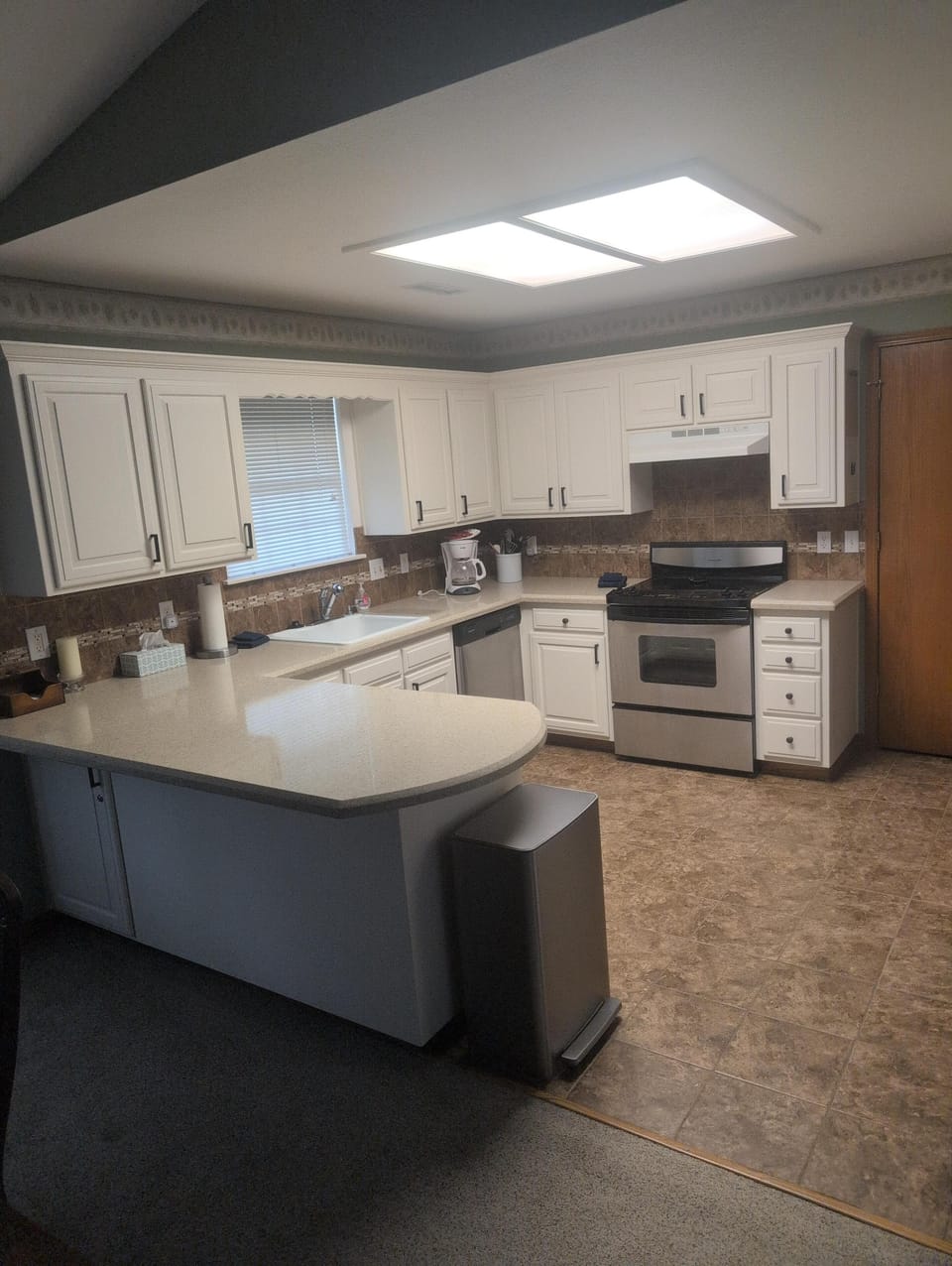 Kitchen with white cabinetry, tiled backsplash, stainless steel appliances, and beige quartz countertop peninsula.