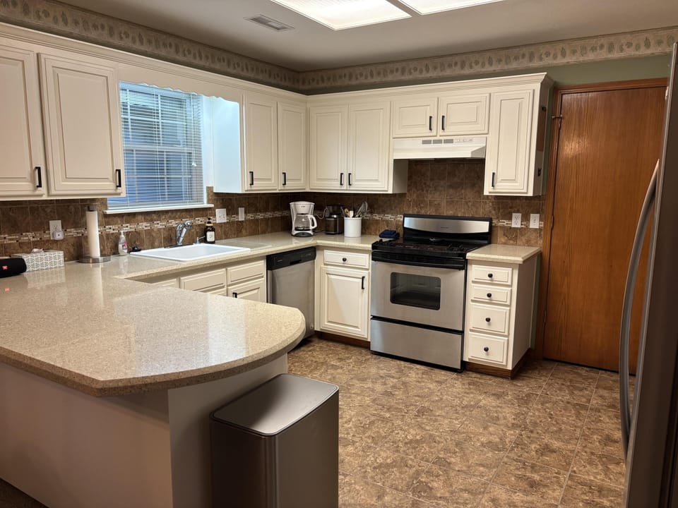 Cream cabinetry contrasts with brown tile backsplash and floor in the kitchen’s U-shaped layout.