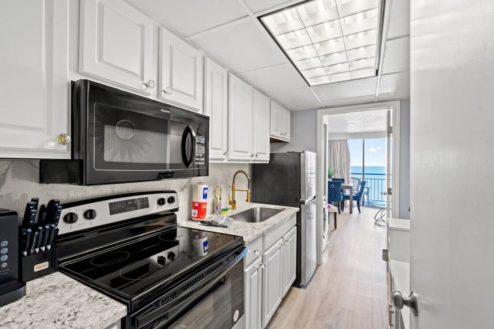 Fully equipped kitchen featuring refrigerator, stove, oven, microwave, freezer, sink, cookware, dishware, and silverware—everything needed for easy meals during your beach stay.