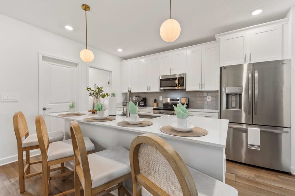 Sleek white kitchen with quartz counters, stainless appliances, and a breakfast bar for 4-fully equipped for morning coffee to family feasts.