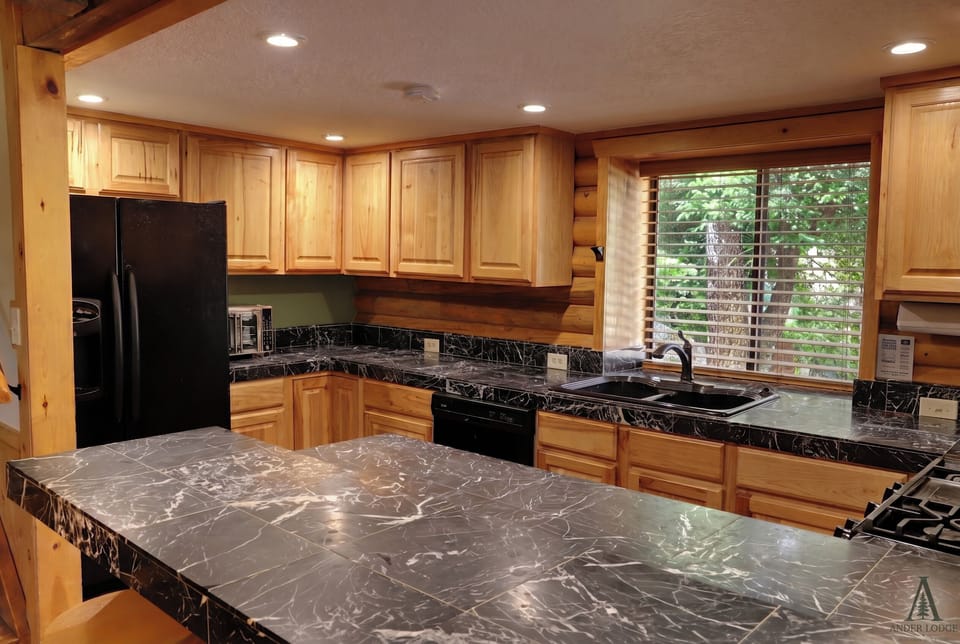 A fully equipped kitchen with knotty alder cabinetry, black granite counters, and an island with cooktop — everything you need to cook a real meal without leaving the mountain.