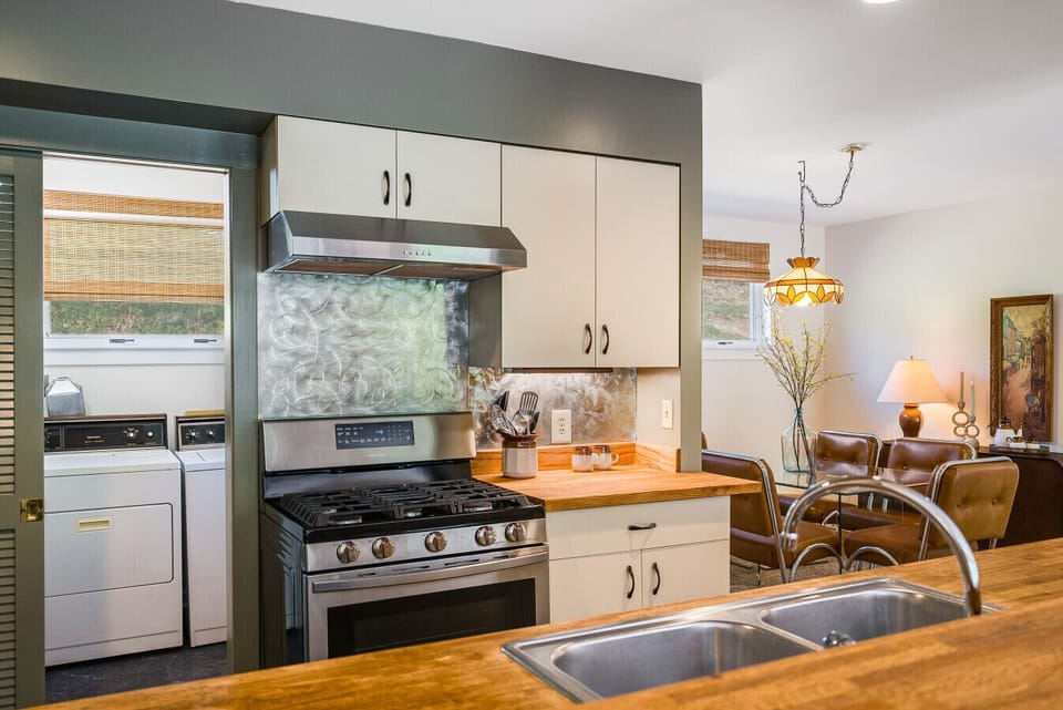 A well-appointed kitchen featuring a modern gas range, butcher block countertops, and an adjacent laundry room with a full-size washer and dryer for guest convenience.