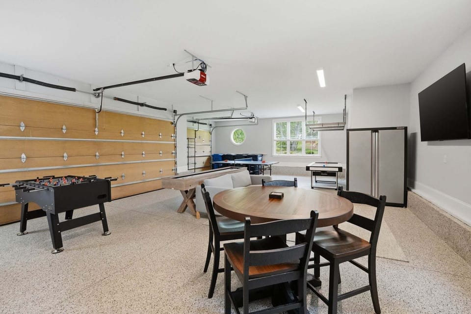 Garage converted to a game room with ping pong, foosball, air hockey, shuffleboard, game table, seating area and TV.
