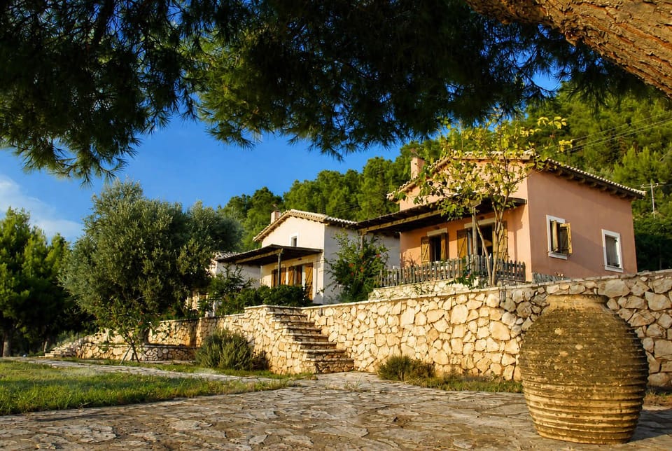The exterior reflects the character of the area, with stone walls, warm tones, and surrounding greenery. The house sits comfortably within the landscape, just above the coastline and close to Egremni Beach.
