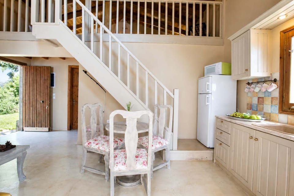 The open-plan living space feels light and easy, with the staircase leading to the attic sleeping area. Natural light moves through the room, connecting indoor comfort with the outdoor setting and sea beyond.