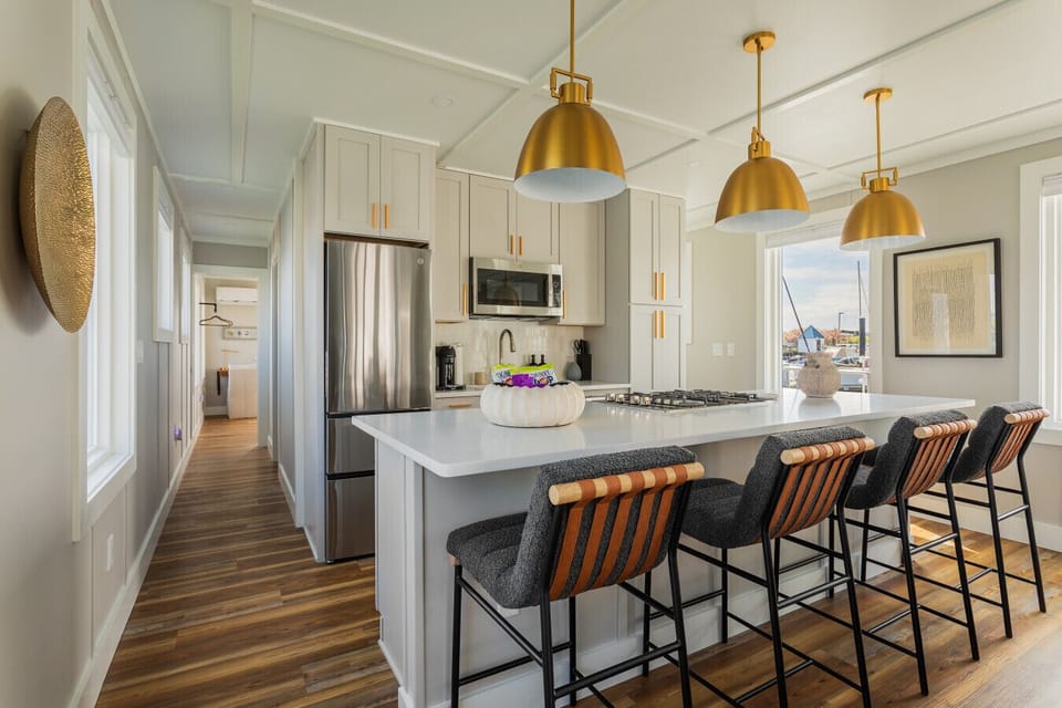 A fully equipped kitchen with a quartz island, gas cooktop, stainless appliances, and four bar stools — ready for everything from morning coffee to a full dinner spread.