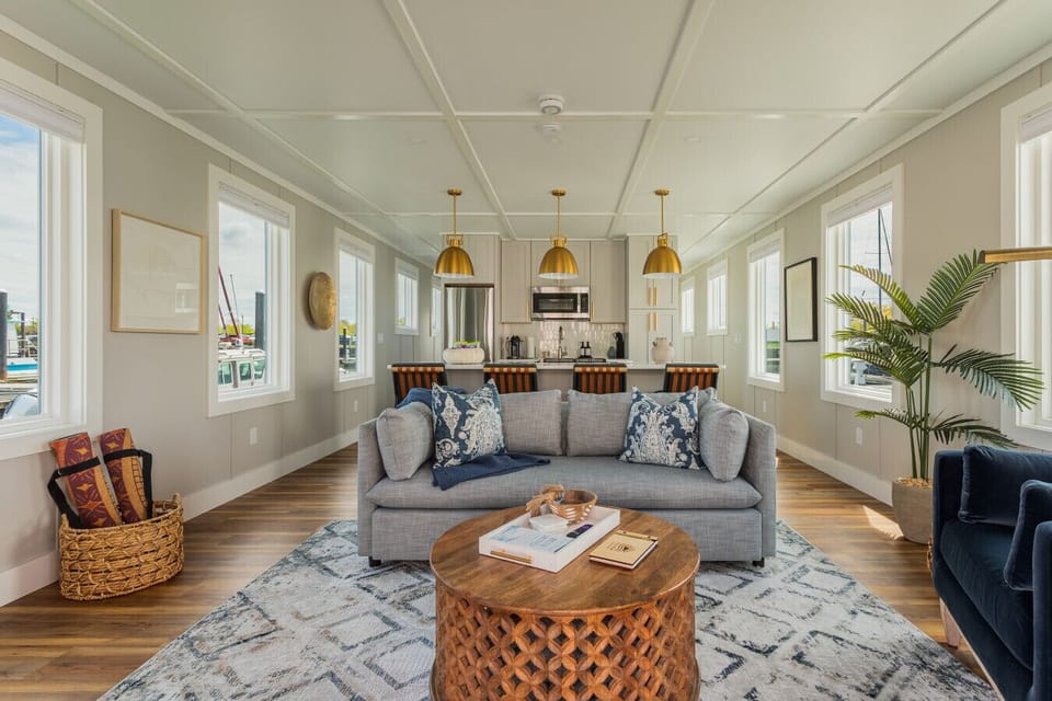 An open-concept living and kitchen area designed with brass pendant lighting, wide-plank hardwood floors, and marina views framing every window.