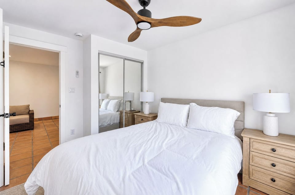 Your serene bedroom retreat features crisp white linens, warm wood accents, and a soothing ceiling fan to keep you comfortable throughout your stay.