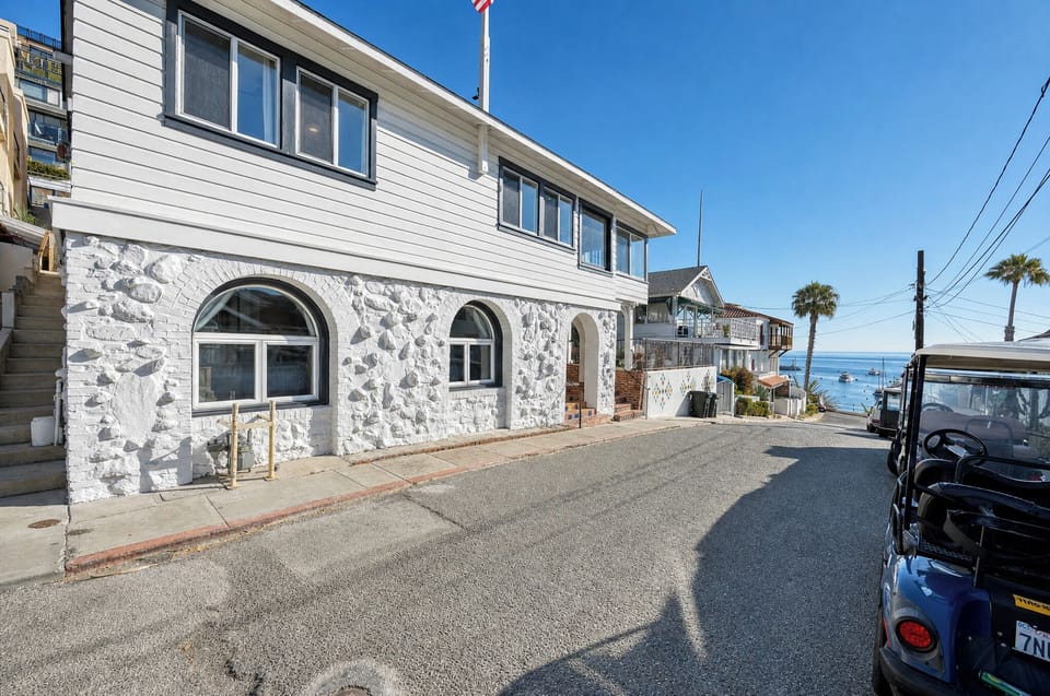 Charming coastal property featuring distinctive white stone architecture on a peaceful residential street, with stunning ocean views just beyond.