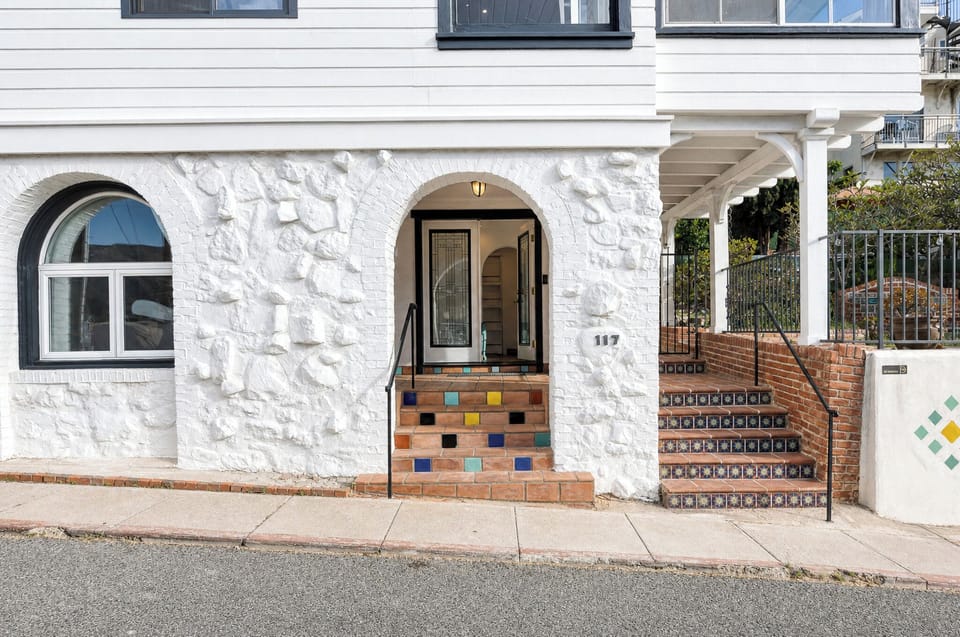 Charming Mediterranean-style entrance features white stone walls, an arched doorway, and colorful hand-painted tile steps with decorative mosaic accents—a welcoming introduction to this unique property.