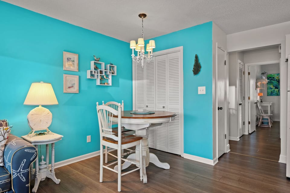 Relax at your charming dining table beneath coastal décor and soft chandelier light. The bright turquoise walls and beachy touches invite you to unwind and enjoy meals in a space that feels like a seaside escape.