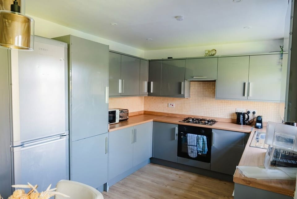 Full kitchen with gloss cabinets, tall fridge freezer, and all appliances.
