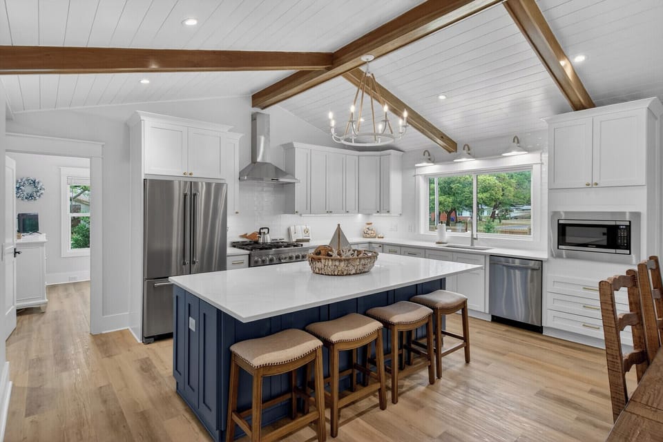 Your spacious chef's kitchen features white cabinetry, navy island with seating, stainless appliances, and beautiful exposed beam ceiling.