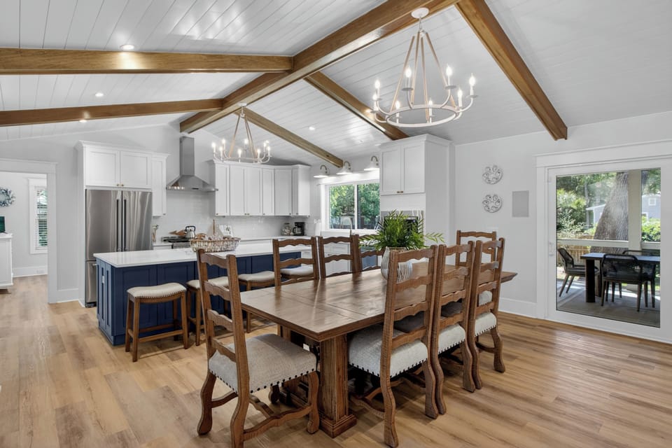 Gather around your stunning dining table beneath vaulted ceilings with warm wood beams. The open kitchen invites you to cook and connect, while natural light streams through glass doors leading to your private outdoor space.