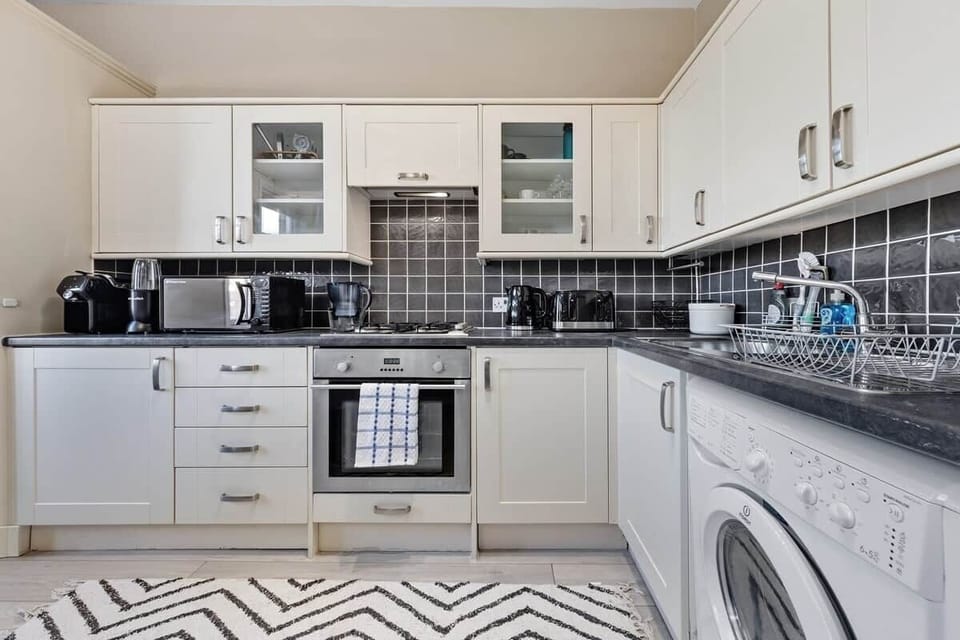 Fully equipped modern kitchen featuring hob, electric oven, microwave, kettle, and fridge/freezer, complemented by a Lavazza coffee machine, NutriBullet blender, rice cooker, washer dryer all for a convenient and comfortable home-from-home stay. 