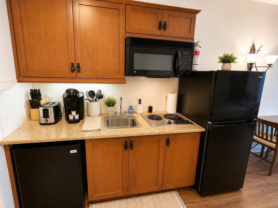 Compact kitchenette with granite countertop, black appliances, maple cabinets, and a small stainless steel sink.