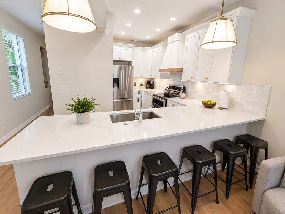 Modern, fully equipped kitchen with sleek white cabinetry, stainless steel appliances, and a spacious island with bar seating—perfect for cooking, dining, or entertaining. Bright lighting and an open layout make it the heart of the home.