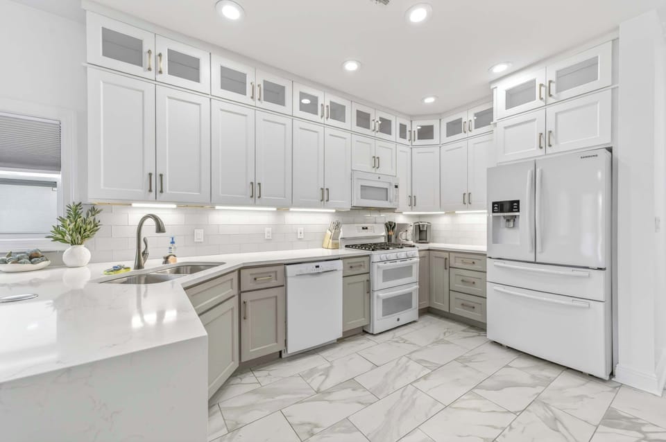 Modern Two-Tone Kitchen

A stylish modern kitchen showcasing two-tone cabinetry with white uppers and taupe lowers. Bright quartz countertops with a subtle marble vein finish complement white appliances and glass-front display cabinets.