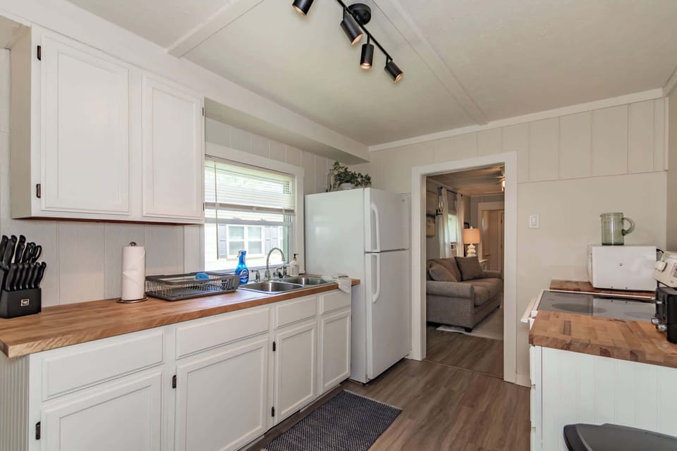 Modern, full-service kitchen with butcher block countertops, a double sink, and white cabinetry. Includes a full-sized refrigerator and an electric range, perfect for preparing family meals.