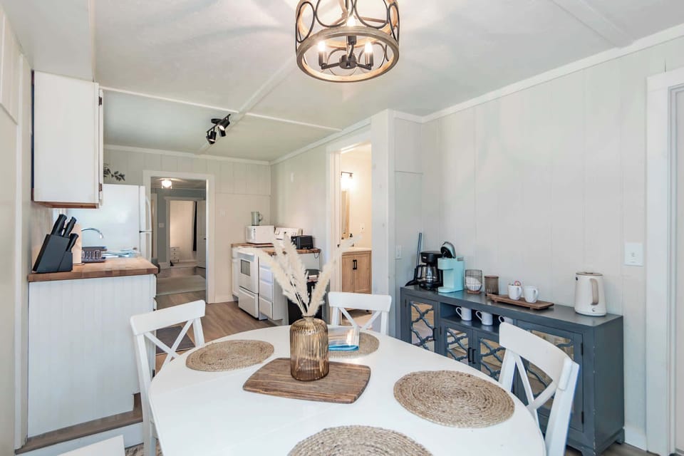 Modern dining area with seating for four, located right next to the coffee bar and kitchen. The space is illuminated by a chic farmhouse-style chandelier, perfect for shared meals.