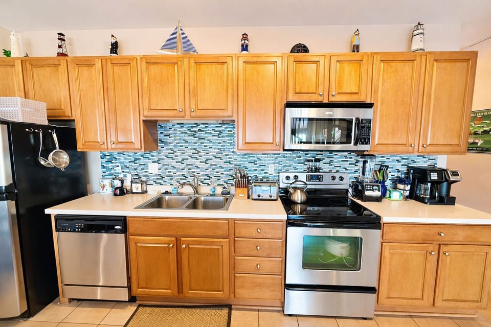 Modern kitchen featuring stainless appliances, double sink, coffee maker, and ample counter space. Nautical accents and warm cabinetry create a welcoming place to cook and connect.