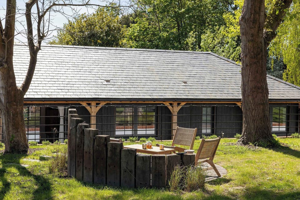 Sip morning tea beneath tall trees, with rustic seating tucked beside a tranquil countryside lodge.