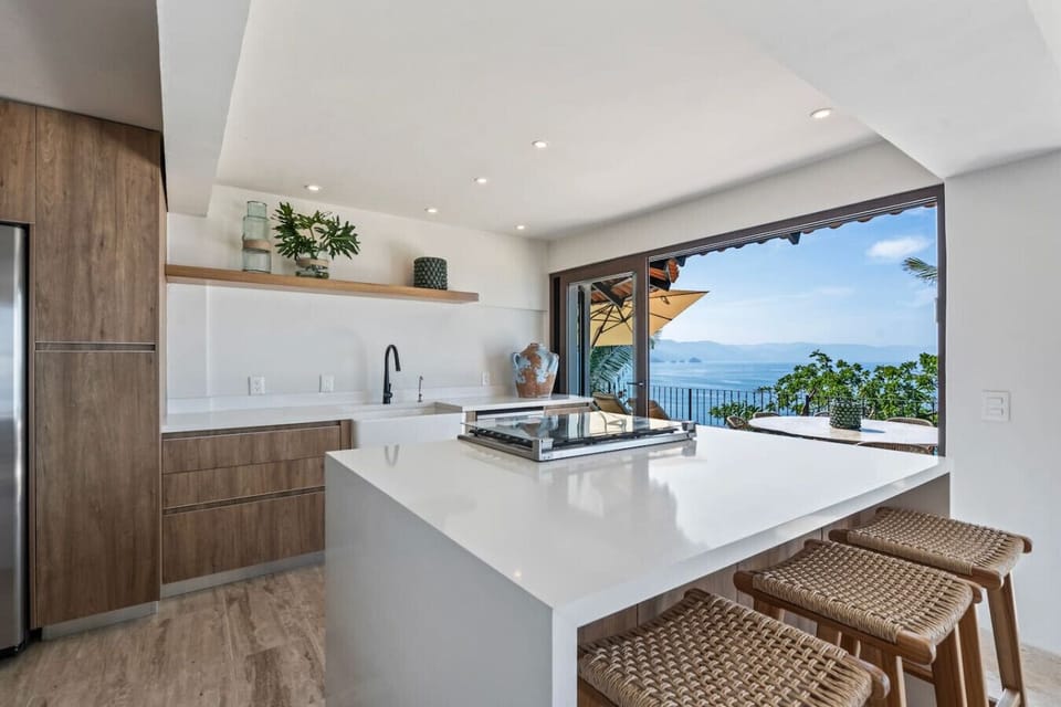 Savor breakfast with ocean views in this sleek Puerto Vallarta kitchen. This luxury rental near Playa Conchas Chinas features a chef island and a beautiful dining area on the balcony, perfect for your next family vacation or remote work
