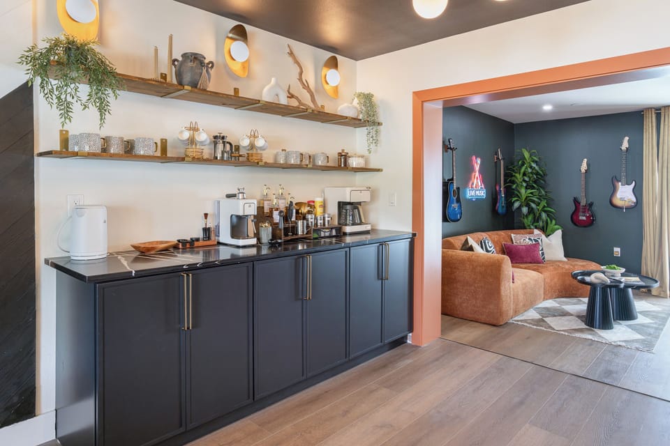 Coffee & beverage station with open wood shelving, espresso machine & drip coffee maker — opens straight into the neon-lit music lounge