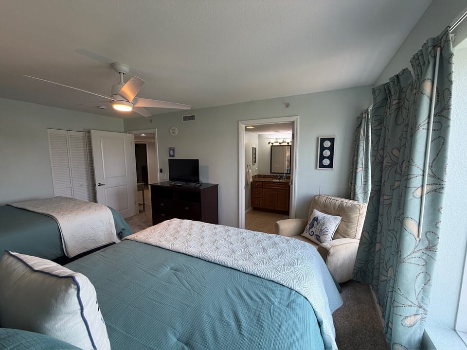 Relax in your coastal-themed bedroom with twin beds, ceiling fan, and cozy seating area for peaceful evenings.