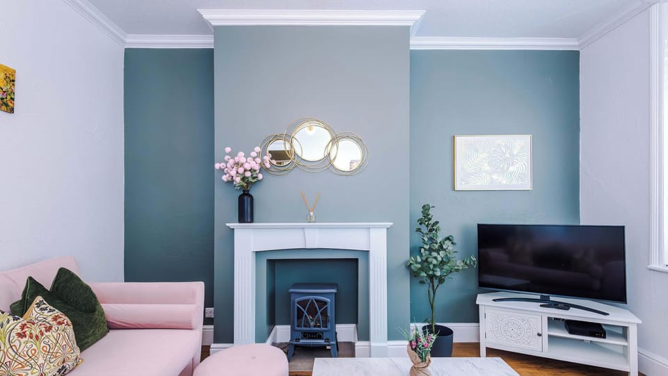 A living room with a pink sofa facing a white fireplace and a television stand.