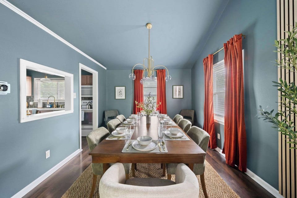 Dining room w/ bold red curtains, a wood table & seating for a full group.
