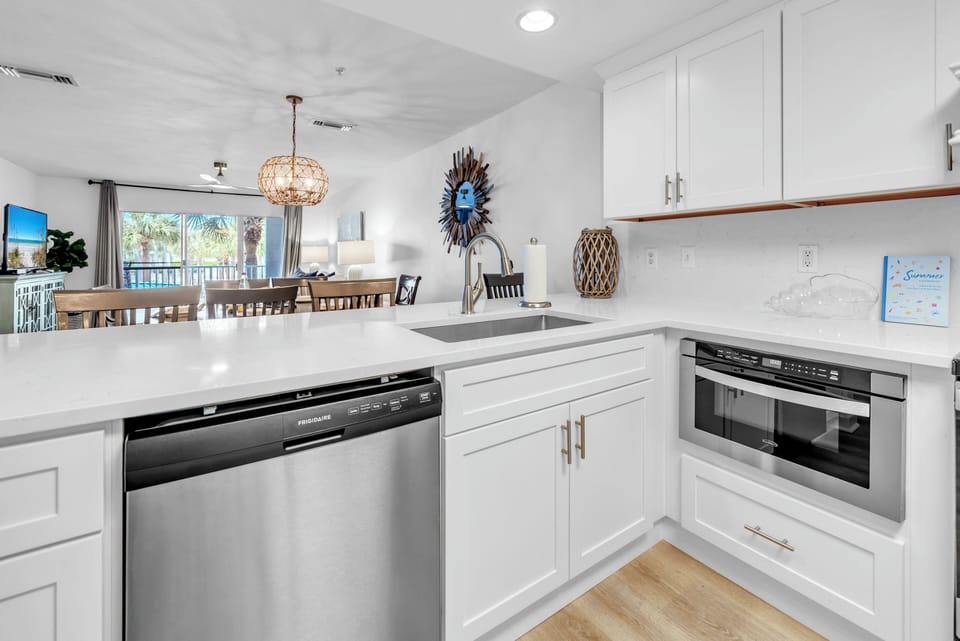 Your sleek white kitchen features stainless steel appliances, quartz countertops, and opens to the bright dining area where palm trees frame your tropical escape.