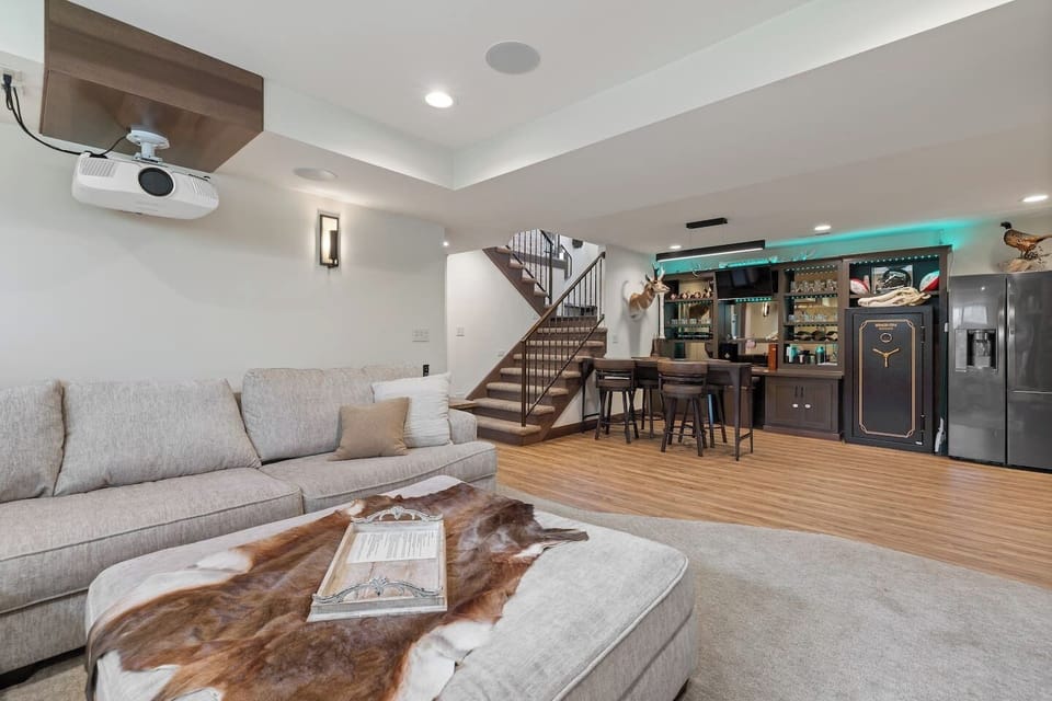 A versatile lower-level entertainment space featuring a sectional seating area, dining setup, and bar, designed for fun and memorable nights in.