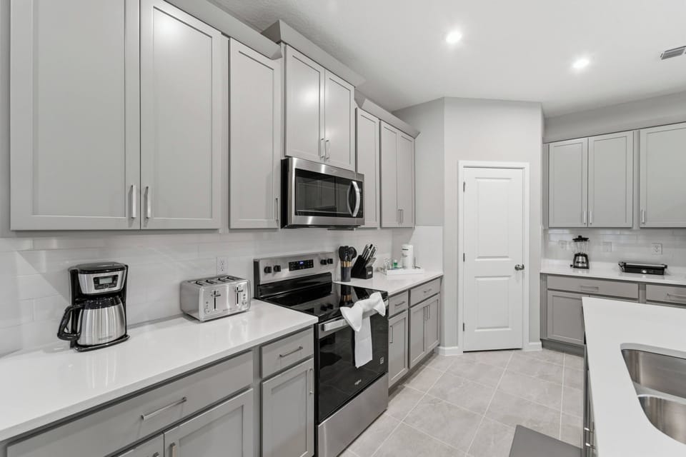 Cook with ease in a modern kitchen featuring bright countertops, gray cabinetry, stainless steel appliances, a large island, and all the essentials for preparing meals during your stay.