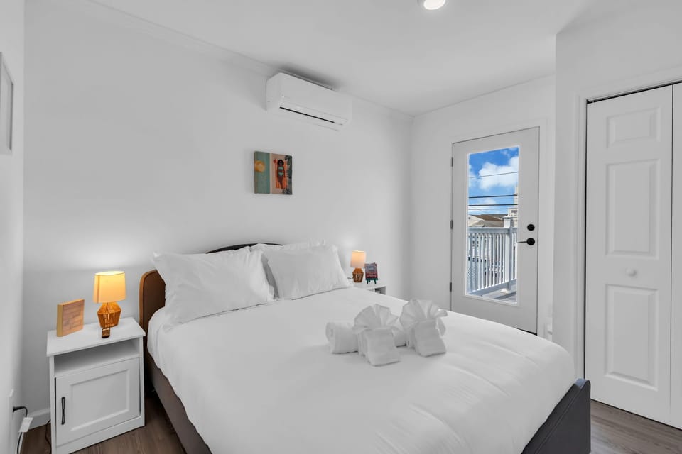 Bright bedroom with queen bed, balcony access, crisp linens, and A/C.
