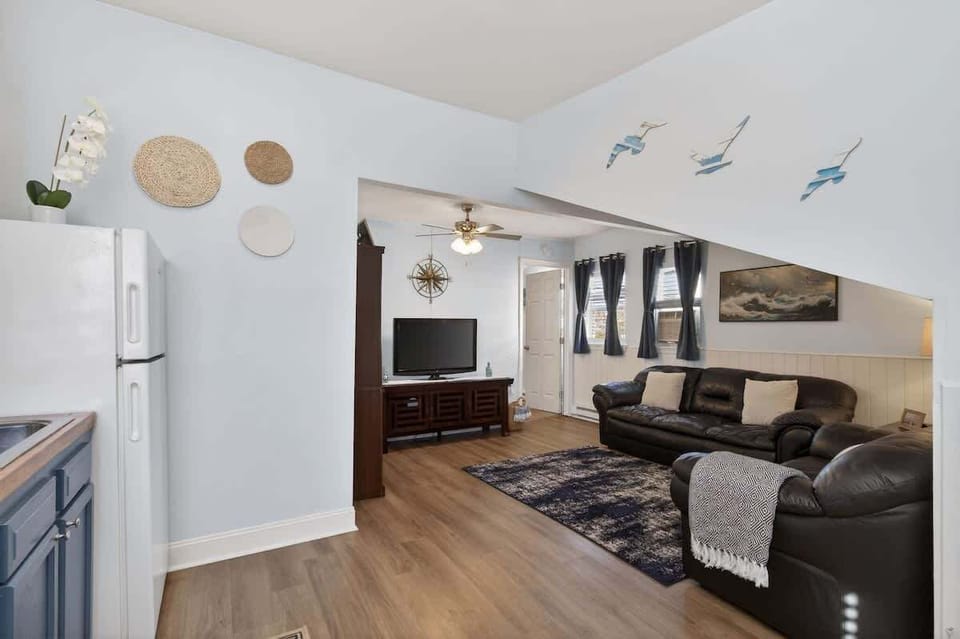 Open layout connecting the kitchen and living room, featuring black leather seating, coastal decor, and a bright, airy feel throughout.