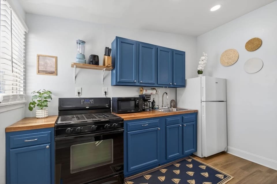 Compact and functional kitchen with blue cabinetry, full-size stove, microwave, coffee maker, and refrigerator—perfect for preparing meals with ease.