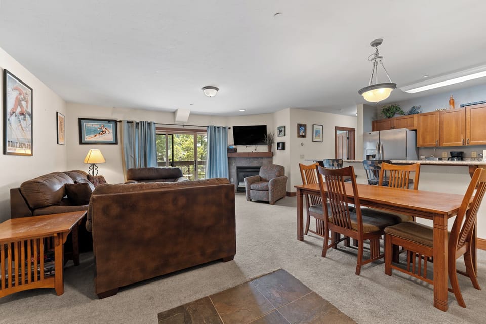 Settle into your spacious open-concept living area, where cozy leather seating flows into a dining space perfect for family meals. Natural light floods through large windows, while the fireplace adds warmth for mountain evenings.