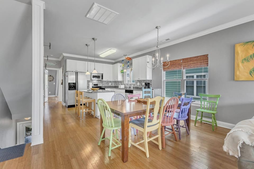 Your open-concept kitchen flows into the dining area where colorful mismatched chairs create a cheerful gathering spot for family meals.