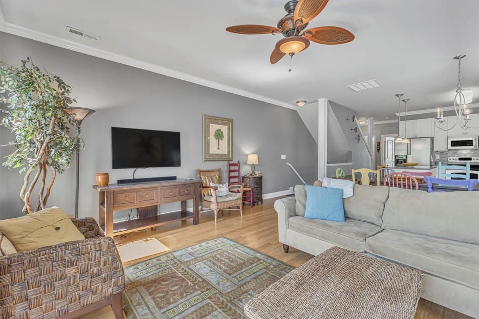 Unwind in your spacious living room with comfortable seating, entertainment center, and tropical ceiling fan creating the perfect coastal retreat atmosphere.