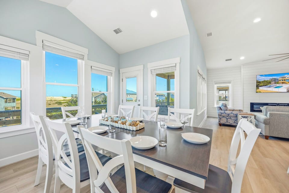 Gather around this elegant dining table, where coastal charm meets effortless style. Large windows bathe the space in natural light, framing beautiful views of the surrounding scenery.