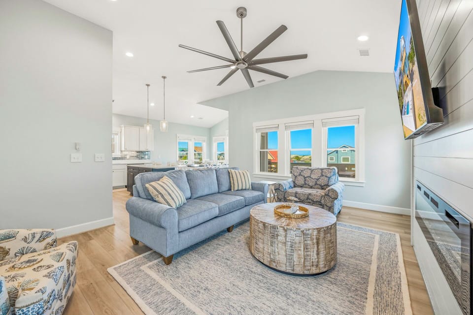 Relax in your airy living room with vaulted ceilings, modern coastal décor, and sunlight streaming through expansive windows overlooking the neighborhood.